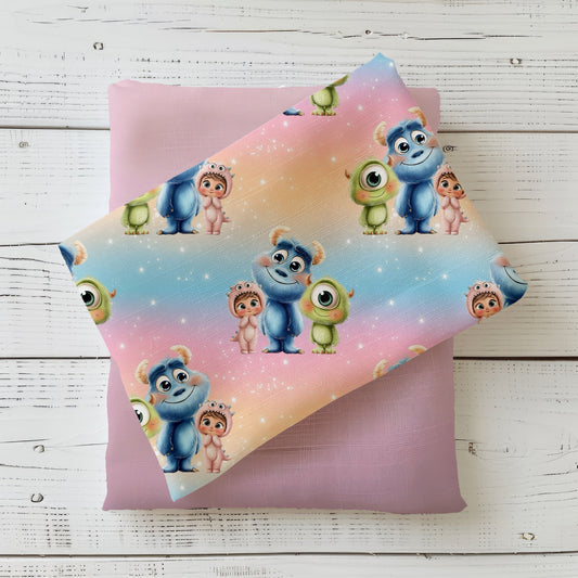 Mockup: Stoff „Monsterfreunde“ mit drei freundlichen Monstern auf Regenbogenverlauf, oben aufgelegt auf einem fliederfarbenen Kombistoff, fotografiert auf hellem Holz.