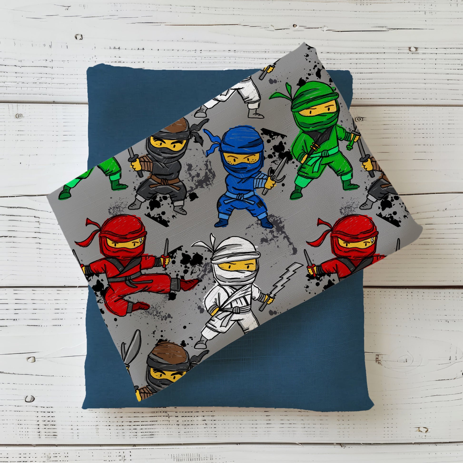 Gefalteter grauer Stoff mit fröhlich bunten Ninjas – modisches und verspieltes Outfit für kleine Action-Fans.