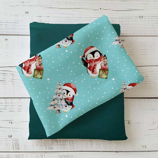 Weihnachtsstoff „Süße Pinguine“ mit niedlichem Pinguin, Geschenken und geschmücktem Tannenbaum auf türkisem Hintergrund.
