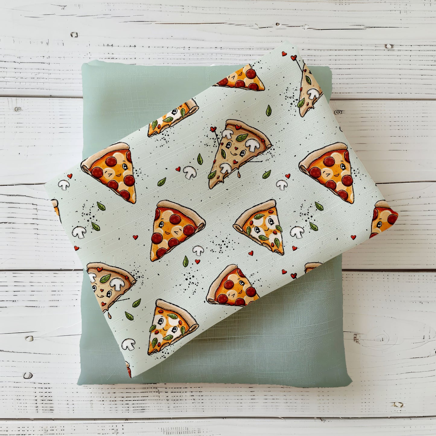 mintfarbener Stoff mit süßen Pizza-Motiven und lachenden Pizzastücken, kombiniert mit Uni-Mint Stoff, auf weißem Holz fotografiert