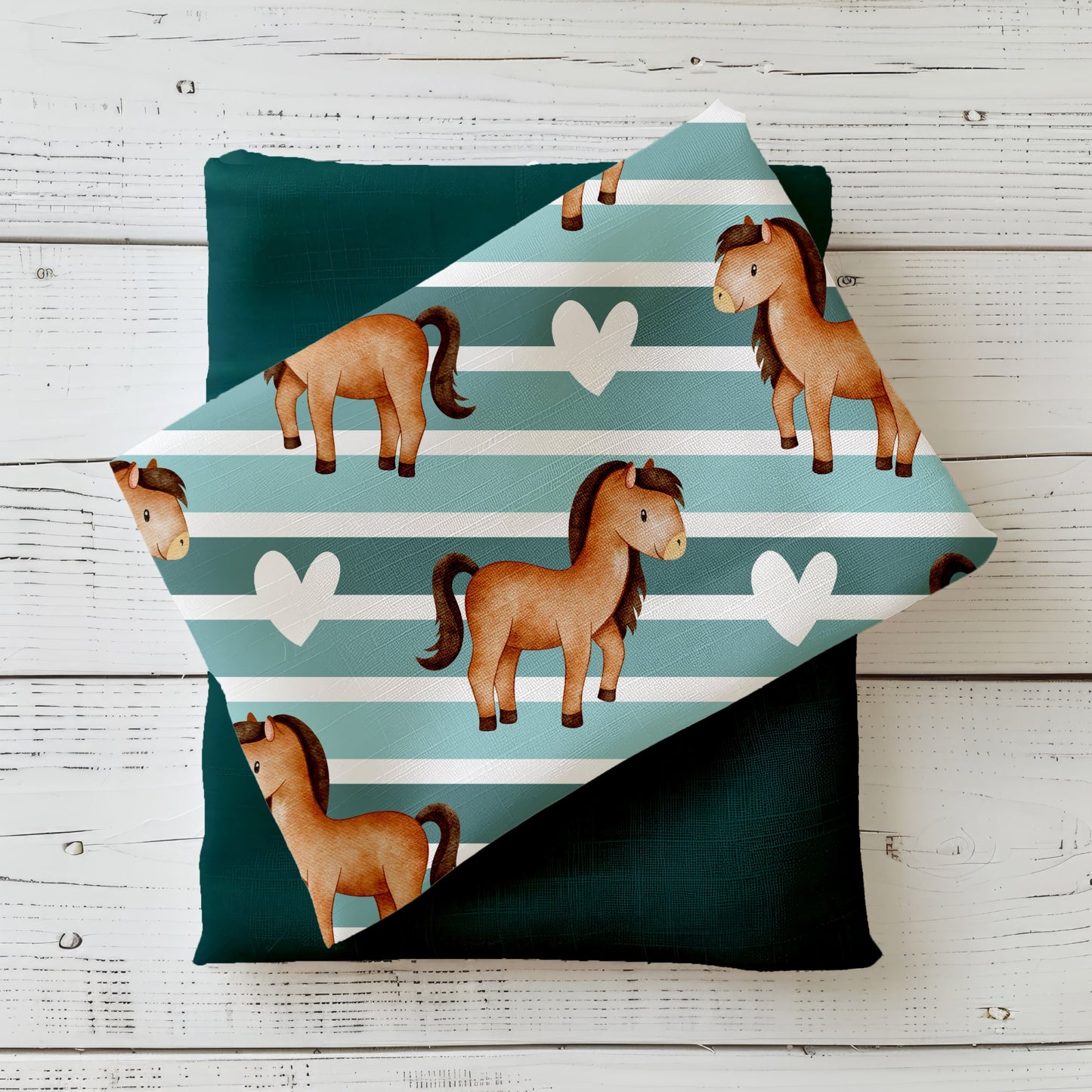 Gefalteter Stoff „Ponyliebe“ mit niedlichen Ponys auf gestreiftem Hintergrund, drapiert auf einfarbigem Kombistoff – Produktmockup auf hellem Holzhintergrund.