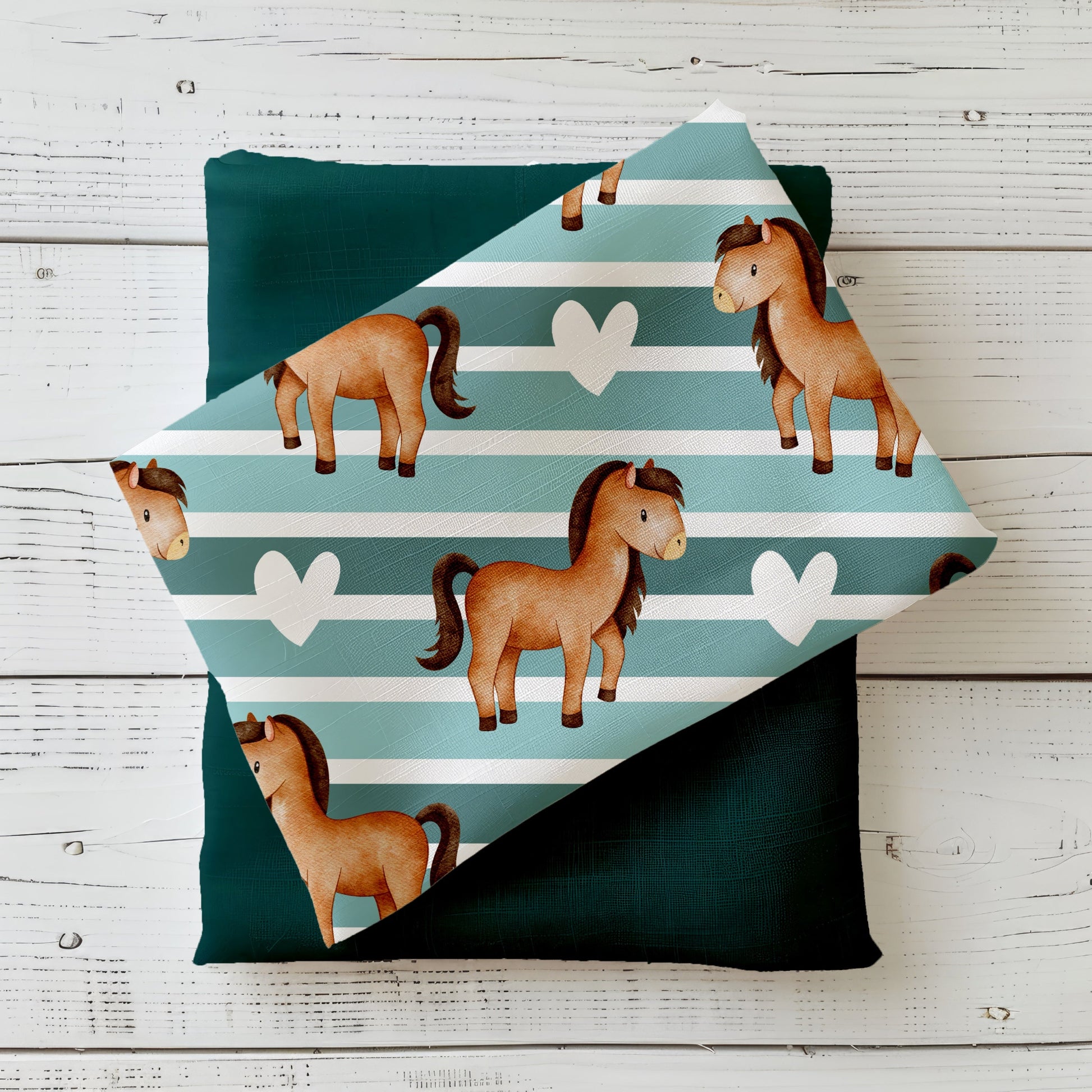 Gefalteter Stoff „Ponyliebe“ mit niedlichen Ponys auf gestreiftem Hintergrund, drapiert auf einfarbigem Kombistoff – Produktmockup auf hellem Holzhintergrund.