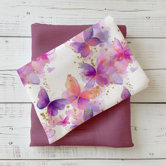 Heller Stoff mit pastelligen Aquarell-Schmetterlingen in Rosa, Violett und Pfirsich sowie goldenen Akzenten – Design „Schmetterlingstanz“: