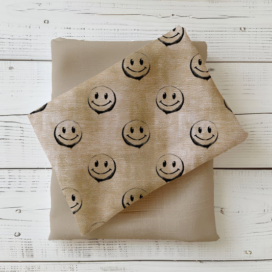 Gefalteter Stoff „Smiley – denim beige“ mit durchgängigem Muster aus violetten Smileys.