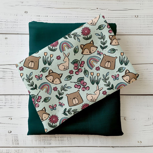 Frühlingsdesign Spring Parts mit Waldtieren, Blumen, Regenbögen und Beeren in sanften Farben, gefaltet präsentiert auf Holzuntergrund