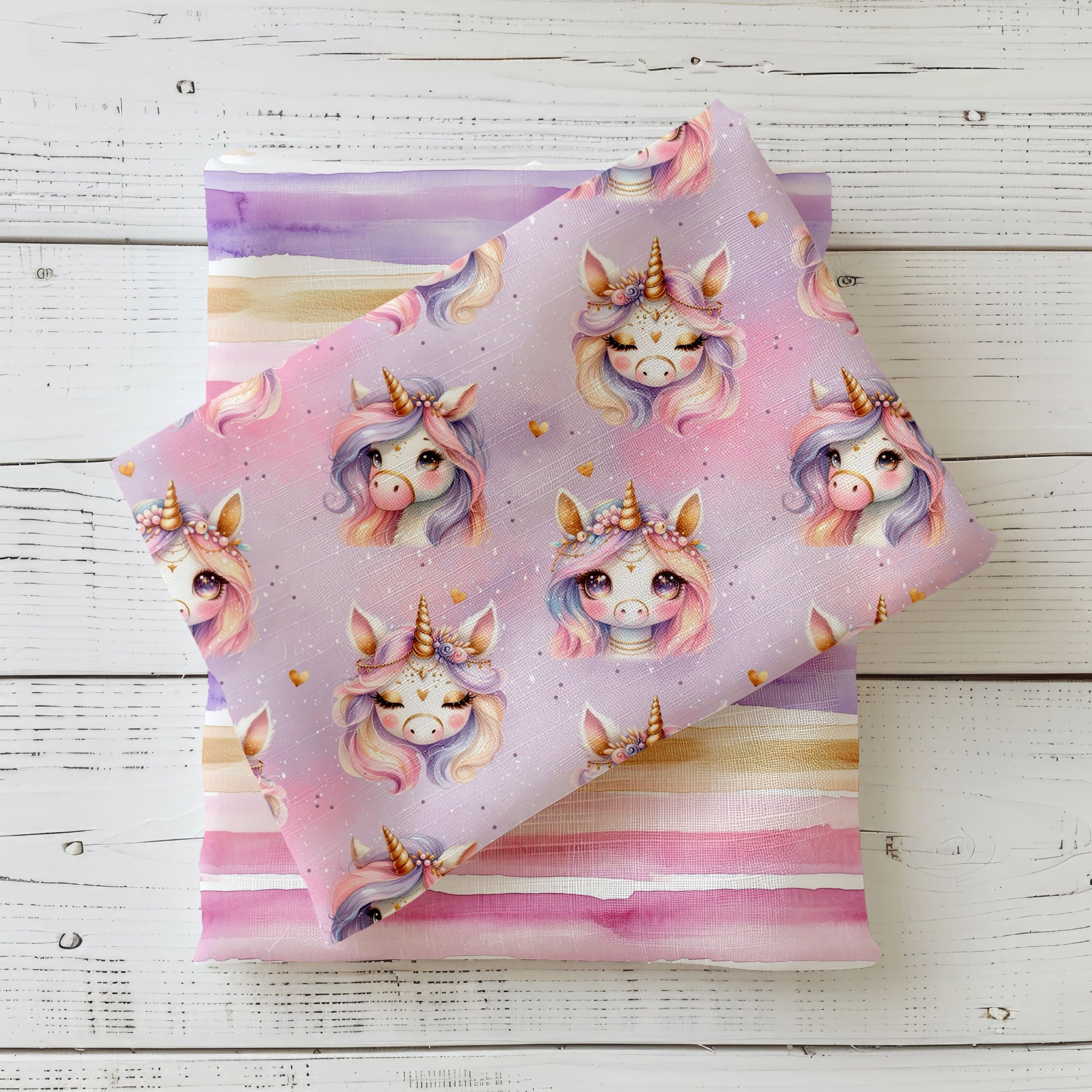 Unicorn Day Stoff dekorativ auf hellem Holzhintergrund drapiert – Einhorn Design in Rosa und Flieder mit Goldakzenten