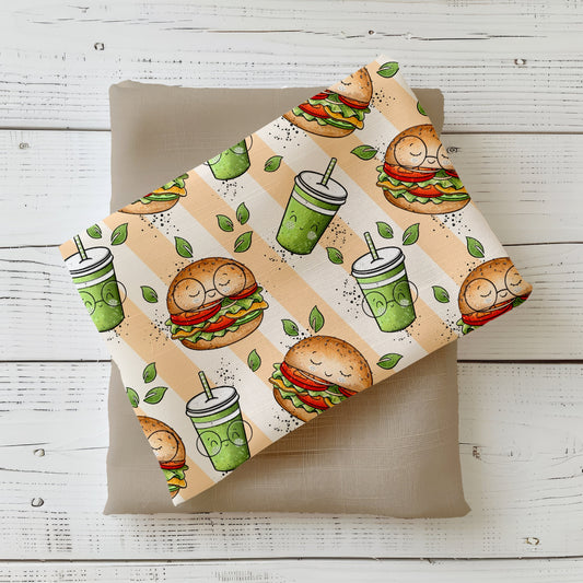 Gefalteter Stoff mit lächelnden Veggie-Burgern, grünen Drinks und Blättern auf beigefarbenem Hintergrund.