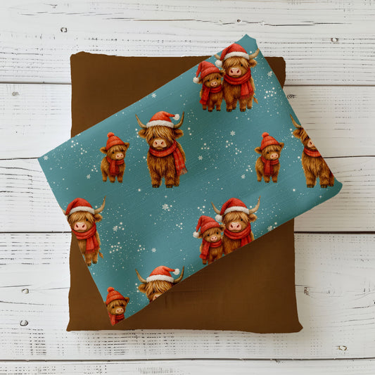 Weihnachtsstoff „Weihnachtskühe“ mit Hochlandrind in Weihnachtsmütze und Schal auf petrolblauem Hintergrund.