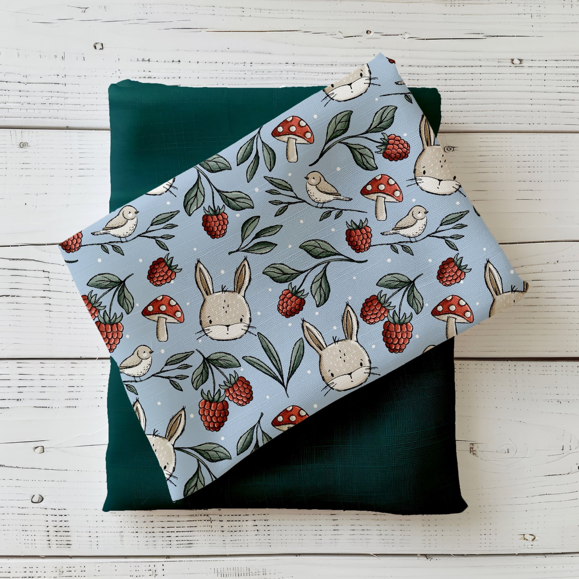Gefalteter „Wiesentag“ Stoff von Katzengold-Designs – Häschen, Beeren, Pilze und kleine Vögel auf blaugrünem Hintergrund, dekorativ auf dunklem Grünton präsentiert