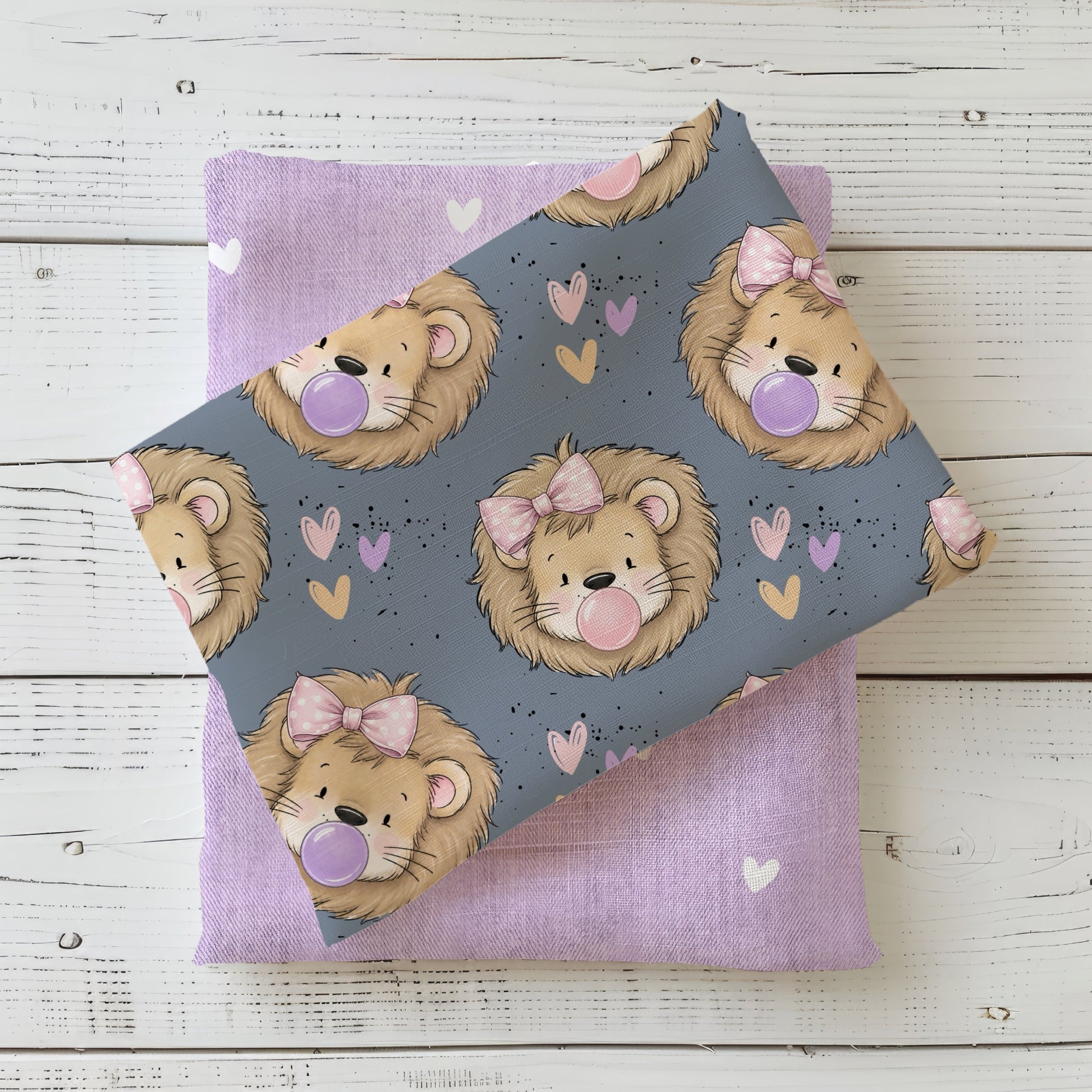 Stoff „Zottellöwe Schleifchen“ mit Löwen, rosa Schleifen, Herzen und Kaugummiblasen auf Graublau, kombiniert mit einem fliederfarbenen Herzchenstoff.