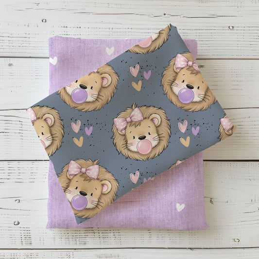 Stoff „Zottellöwe Schleifchen“ mit Löwen, rosa Schleifen, Herzen und Kaugummiblasen auf Graublau, kombiniert mit einem fliederfarbenen Herzchenstoff.