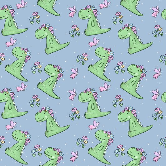 Verspielter Stoff mit Dinosaurier-Motiv „Rexeline“: Grüne Dinos mit Blumenkranz auf dem Kopf, rosa Schmetterlinge und bunte Blümchen auf blauem Hintergrund mit weißen Punkten – ideal für Kinderkleidung.