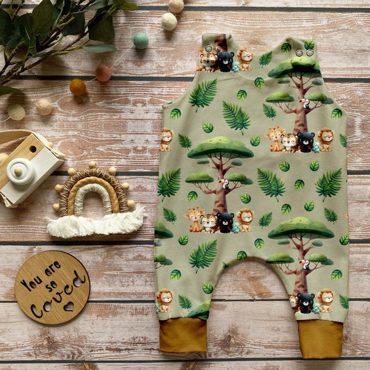 Handgemachter Baby-Strampler im Safari-Design mit Dschungeltieren wie Löwen, Tigern und Giraffen auf beigem Hintergrund, fotografiert auf Holzuntergrund mit Dekoration.