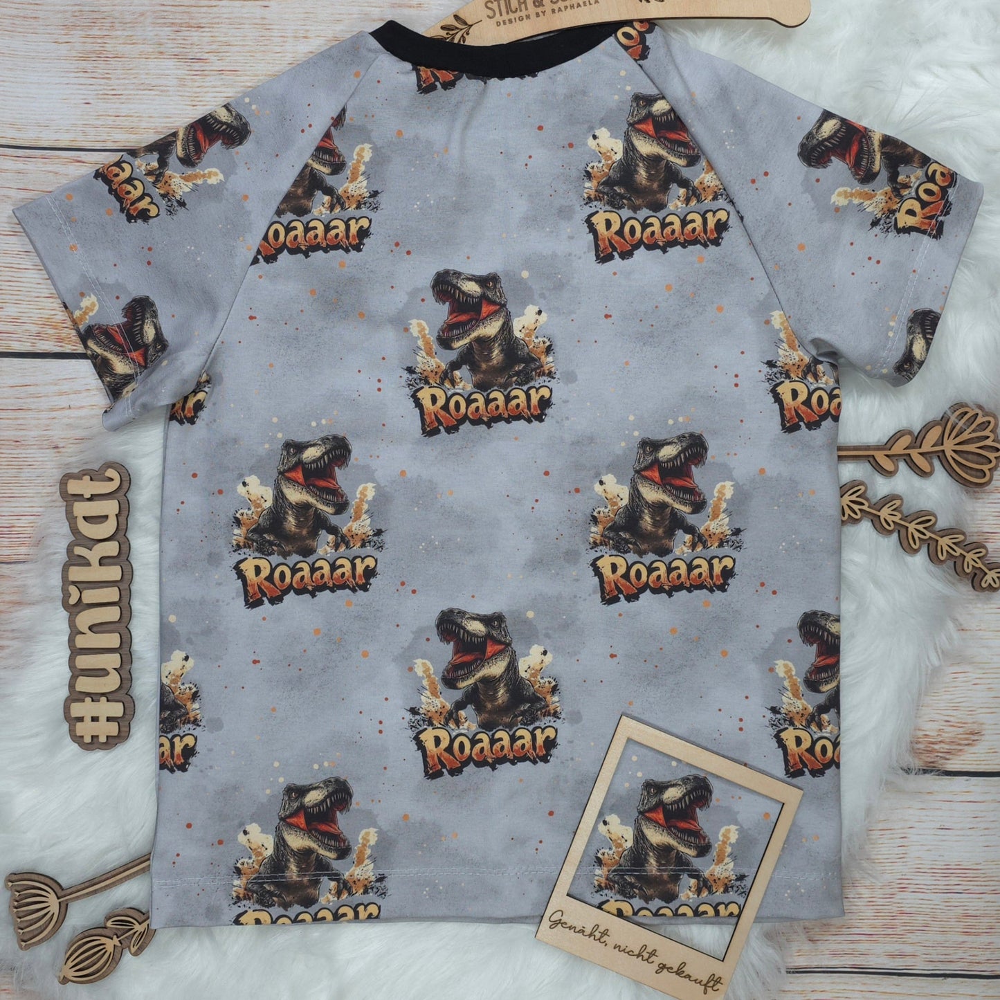 Rückseite des handgenähten Kinder T-Shirts T-Rex in Größe 122 mit Dinosaurier-Allover-Design auf grauem Hintergrund
